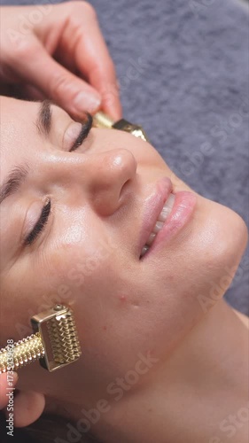 A woman receives a professional facial treatment using luxurious gold rollers to brighten her skin.