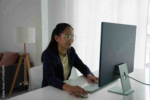Asian Female Accountant Diligently Working on Desktop Computer. Modern Office Setting for Financial Reporting and Analysis, Highlighting Focus and Professionalism.