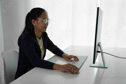 Asian Female Accountant Diligently Working on Desktop Computer. Modern Office Setting for Financial Reporting and Analysis, Highlighting Focus and Professionalism.