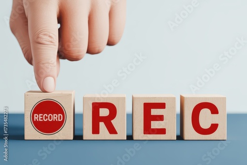 Close-up of a hand pressing a wooden block with a red record button symbol, initiating the start of a recording or process
