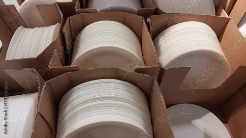 Close-up video of neatly stacked white ceramic plates arranged in cardboard packaging. The footage captures the clean, glossy surface of the plates