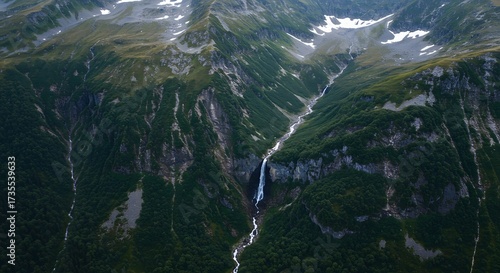 Majestic waterfall flows through rugged valley with snowy peaks dense forest and steep cliffs evoking wild untouched natural grandeur