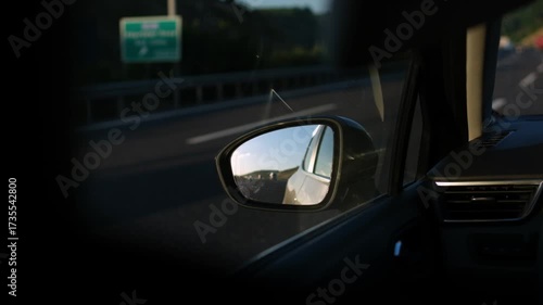 The sun shines on a tranquil highway as a car drives, reflecting the beautiful landscape in the side mirror while a peaceful journey unfolds.