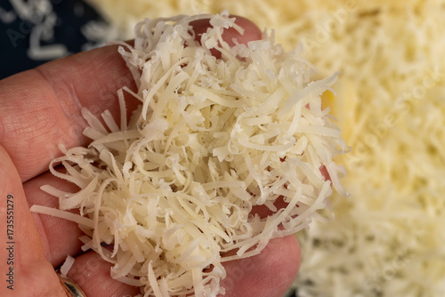 finely grated fresh yellow hard cheese on a metal grater for pizza , yellow grated cheese with pieces for cooking various foods