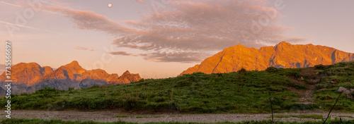 Panoramic alpine meadow at sunset in the Berchtesgadener Alps with wooden hut and glowing mountain peaks