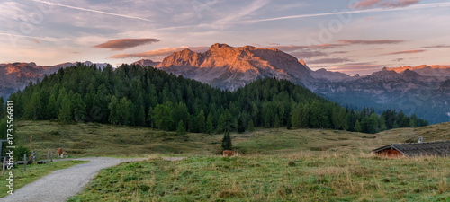 Panoramic alpine meadow at sunset in the Berchtesgadener Alps with wooden hut and glowing mountain peaks
