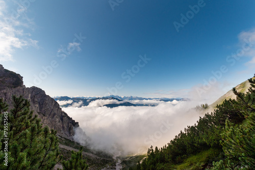 Cloud inversion drifting through rugged alpine landscape under clear blue sky