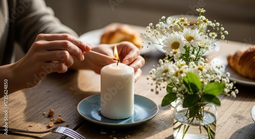 Person lighting a candle on a dining table with flowers and pastries