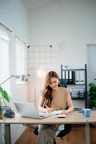 Asian businesswoman multitasking with phone and notebook in bright office. Perfect for business, communication, consulting, productivity, and professional work themes.
