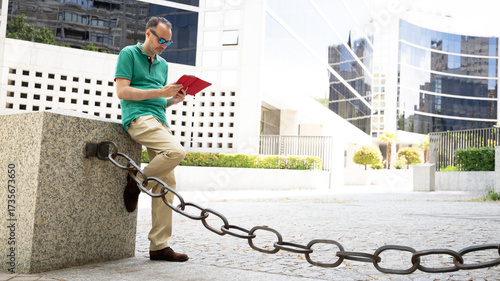 middle-aged man leaning his foot against a wall looking down at his tablet