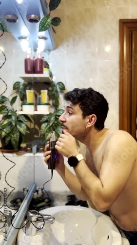 Man shaving beard with electric razor in bathroom mirror