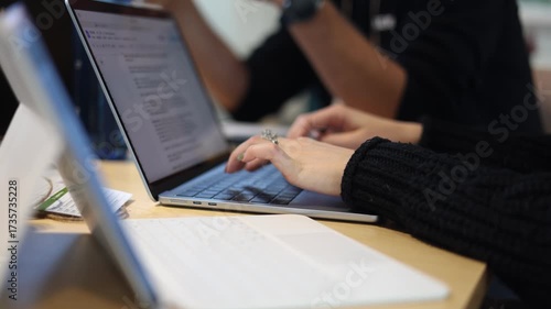 Close-up of hands typing on a laptop keyboard during a collaborative work session, with notes, documents, and colleagues contributing to a focused project