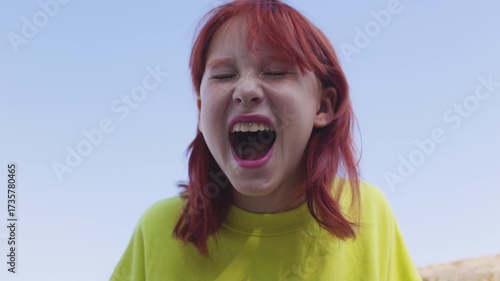 An emotional teenage girl looks at the camera, screams, and expresses her negative emotions by shouting. Teenager screaming. Slow motion.