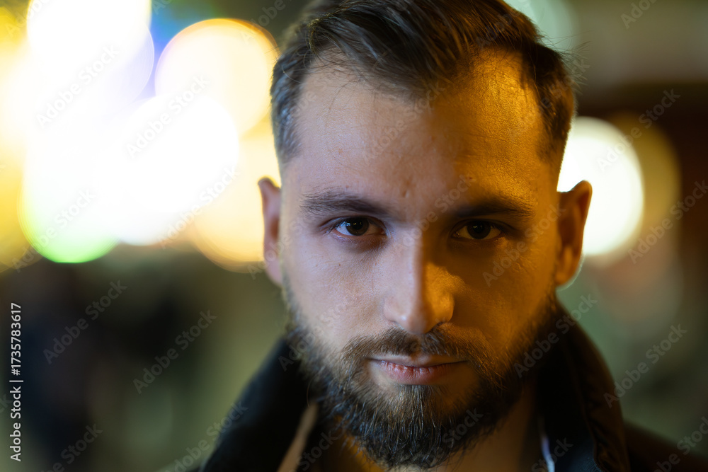 Fototapeta premium Young bearded man gazing directly at urban night