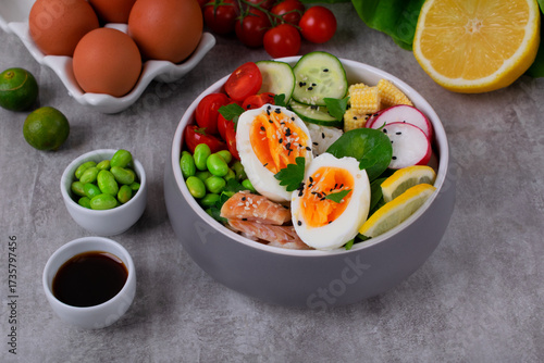 Poke bowl with smoked redfish, eggs, vegetables, edamame beans and rice served on gray table. Healthy balanced meal with white fish