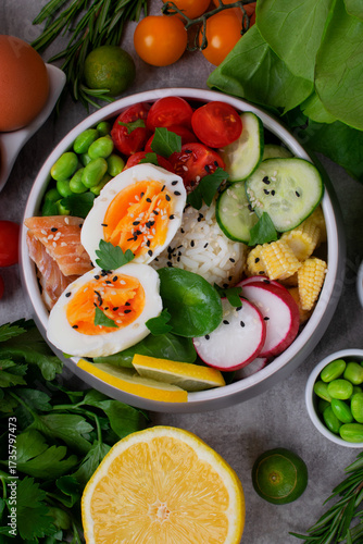 Poke bowl with smoked redfish, eggs, vegetables, edamame beans and rice served on gray table. Healthy balanced meal with white fish. Top view
