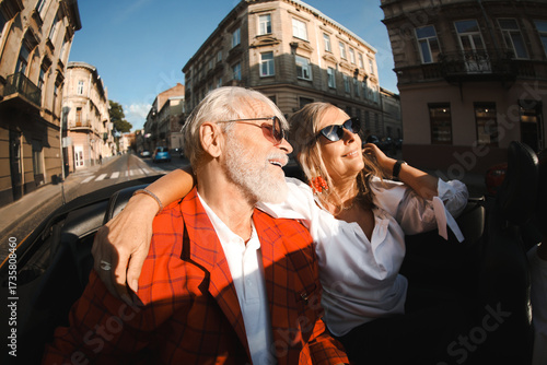 Bild auf Leinwand Senior couple enjoying cabriolet ride in city, wide angle lens