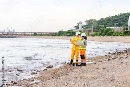 Environmental Engineers Testing Seawater Quality at Coast, Safety Officers Inspecting Coastal Area Near Industrial Port, Two Scientists in Safety Gear Analyzing Data on Beach
