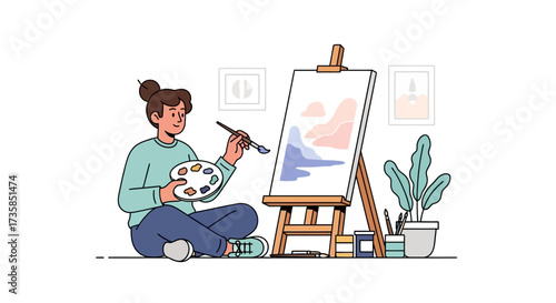 A young woman sits cross-legged, painting an abstract landscape on a canvas supported by a wooden easel in a bright, minimalist studio.