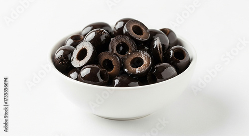 A close up view of a white bowl filled with sliced black olives on a plain white background surface