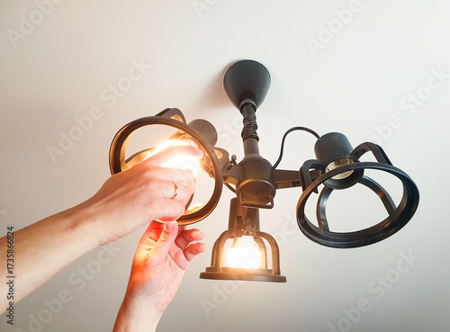A woman screws an LED light bulb into a chandelier by hand, replacing a lamp, home lighting.