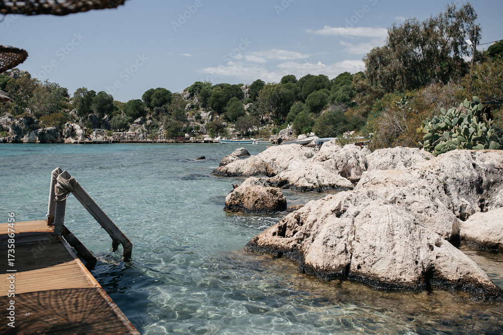 Fototapeta premium Rocks and sea. Peaceful Mediterranean bay: crystal waters and rocky cliffs, steps leading down into the water. Deserted empty beach.
