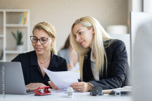 Two women working together at a desk with charts and documents
