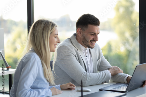 Two colleagues working together at a desk and looking at laptop