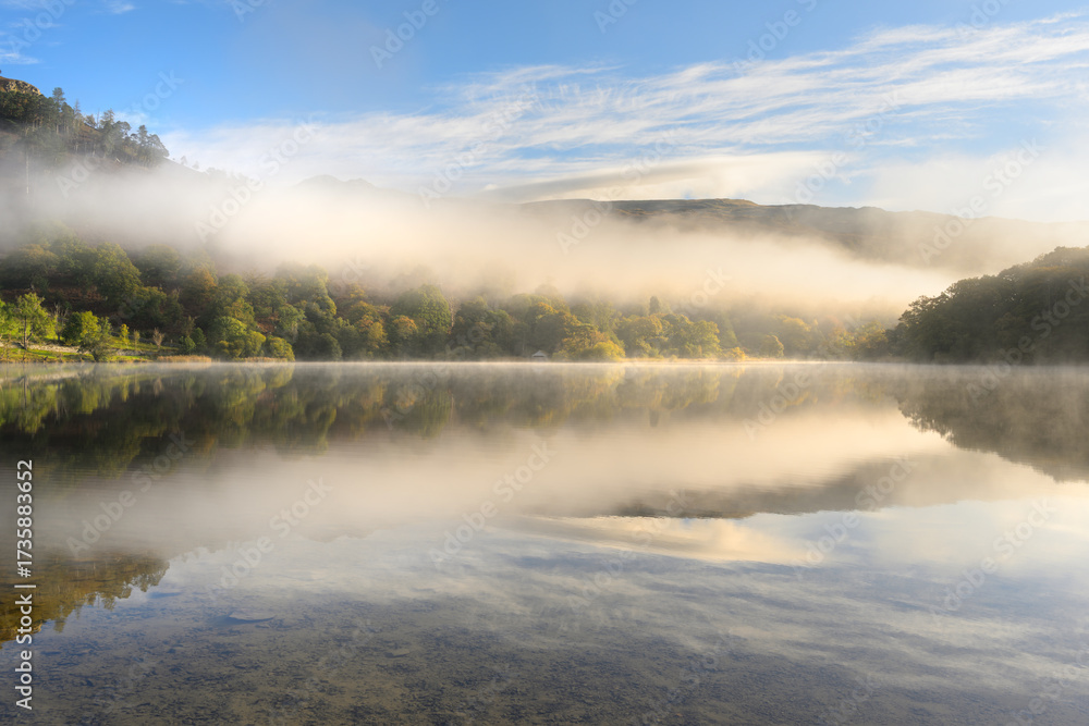 Fototapeta premium Beautiful autumn morning reflections at Rydal Water with golden light and mist in The Lake District, UK.