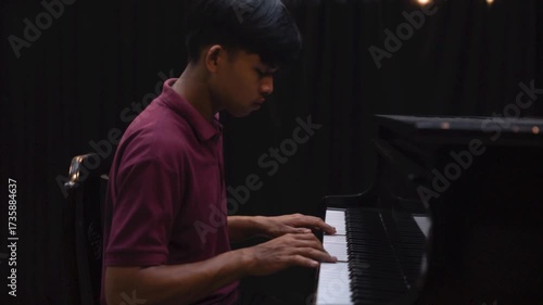 Young Man Playing Grand Piano on Stage Under Dramatic Lighting Music Concert or Recital Scene