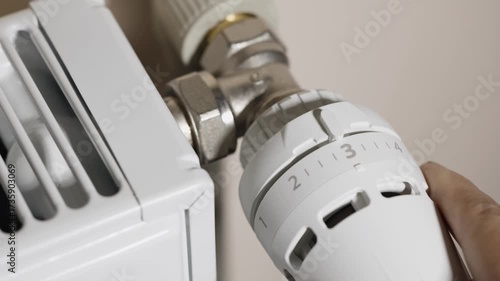 A man's hand adjusts the temperature on a radiator thermostat,