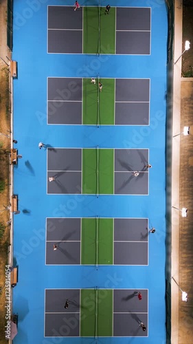 Aerial view of multiple pickleball courts with players in action, top down perspective of sport game, people playing recreational match under lights