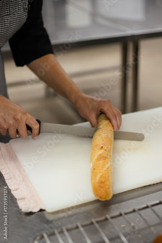 Person slicing fresh baguette on a cutting board in a bakery kitchen
