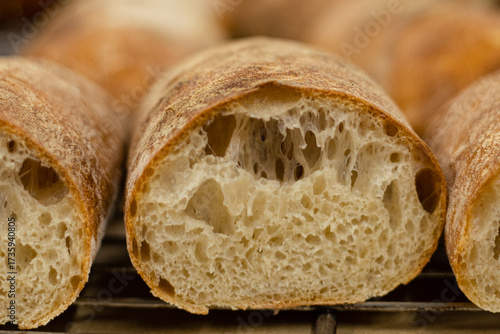 Close-up of freshly baked artisan baguette with golden crust and airy crumb texture. Traditional homemade bread cooling on a rack.