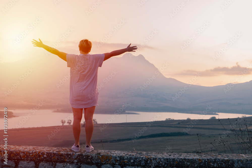 custom made wallpaper toronto digitalPerson stands on stone wall facing glowing sunrise, freedom in open arms, freedom in breath and in wide horizon, mountain silhouette and lake shine under soft morning haze