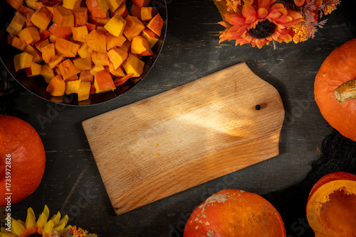 Freiraum auf Schneidebrett aus Holz für Schrift auf Tisch herbstlich dekoriert mit Kürbis und Blumen in Orange