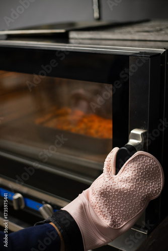 Person wearing oven mitts takes freshly baked focaccia with salt out of the oven.