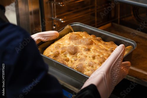 Person wearing oven mitts takes freshly baked focaccia with salt out of the oven.