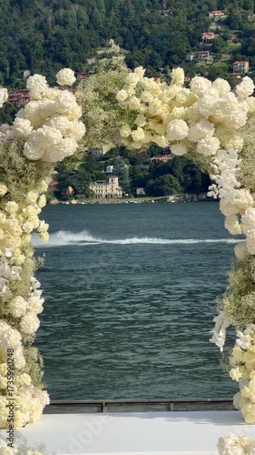 Cinematic drone view of outdoor wedding ceremony at villa on Lake Como, Italy. Yacht passing through floral arch, , scenic lake and mountain backdrop, luxury lakeside event