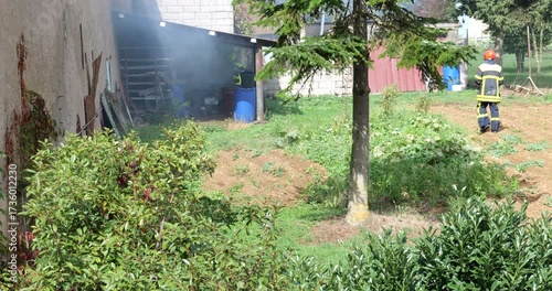 Firefighter responding near a smoking house. Firefighter in action in a residential garden. Firefighter standing in garden after small house fire