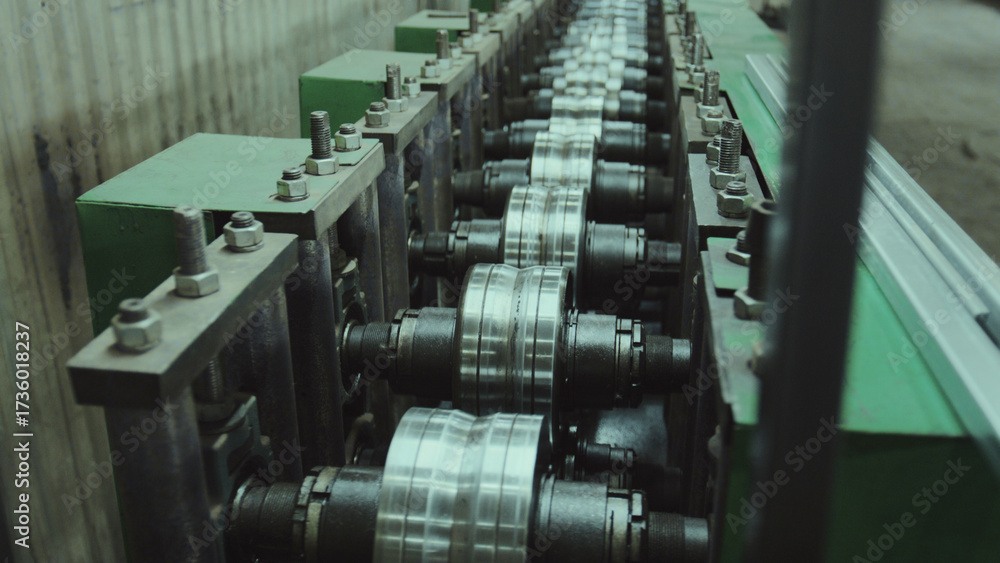 Obraz premium Industrial equipment with a series of mechanical rollers shaping long metal sheets into specific profiles, showcasing the manufacturing process in a steel processing factory