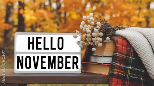 Cozy hello november lightbox sign with stacked books and warm plaid blanket against a blurred autumn forest background