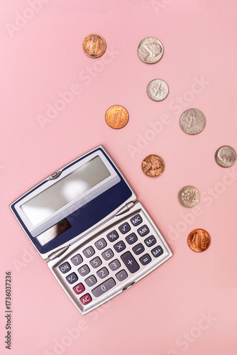 flat lay of a compact calculator and scattered change including dimes, pennies, quarters, and nickels against a pink background in a vertical orientation