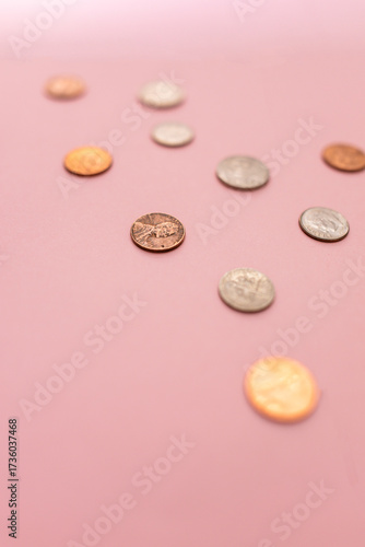 close-up of change including pennies, nickels, and dimes against a pink background blurred in a vertical orientation 