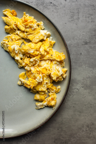 close-up of freshly scrambled eggs on a gray plate against a gray background, breakfast