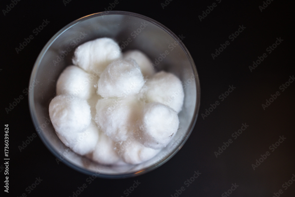 Fototapeta premium Close-up of fluffy clean white cotton balls in a clear jar against a dark background with copy space 