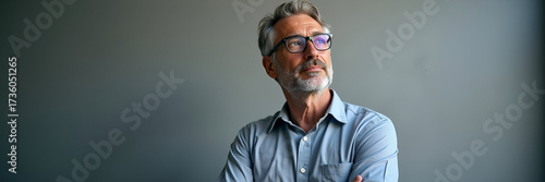 A confident middle-aged man gazes thoughtfully away at a gray office wall, embodying inspiration and ambition; accompanied by generous copy space to insert text or logos.