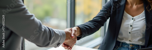 A joyful young female bank manager establishing rapport with a client through a handshake during a meeting, symbolizing partnership and trust in a corporate environment, providing generous room for te