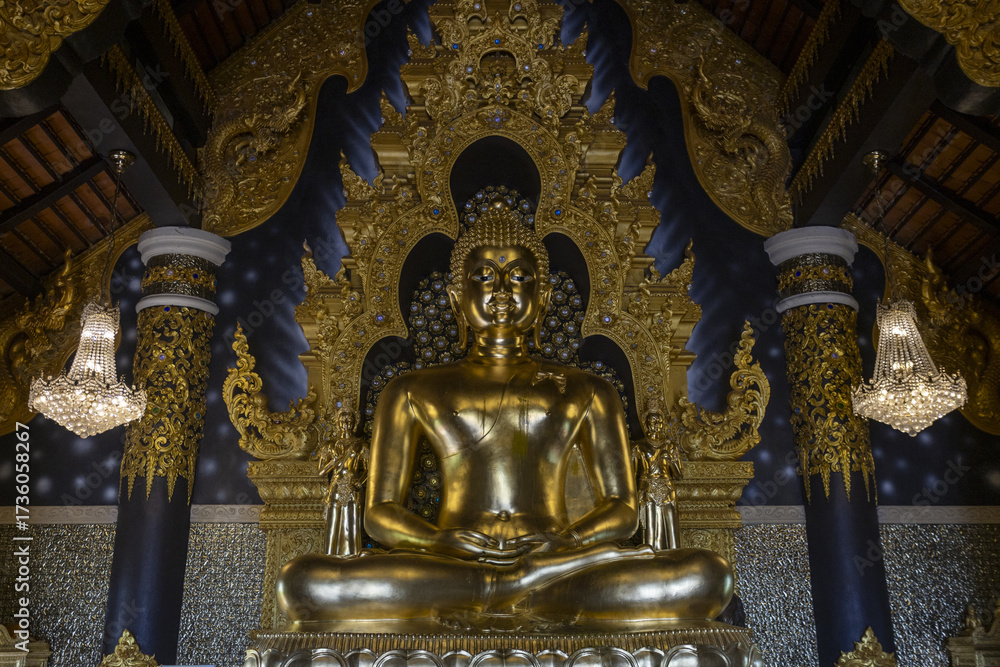 Fototapeta premium Serene golden Buddha statue sits peacefully within richly decorated temple interior, surrounded by intricate gold carvings and dark blue walls. sacred space exudes profound tranquility