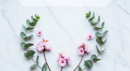 Pink blossoms and green eucalyptus leaves arranged on a white marble surface forming an elegant floral border
